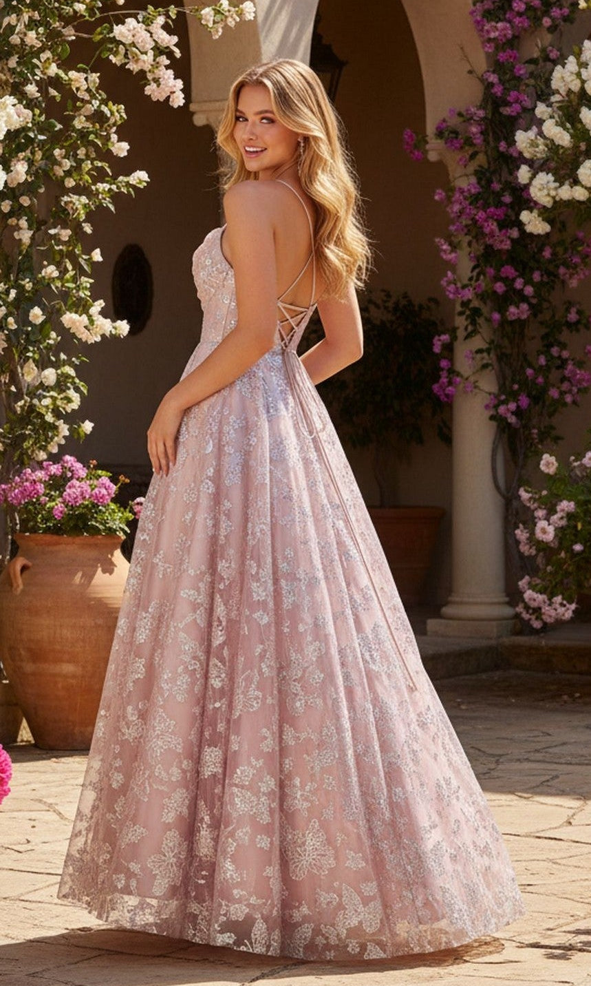 A woman in the Blondie Nites 6007BN long prom dress, featuring a light pink corset bodice and lace-up back, stands outdoors by flowers and terracotta pots.